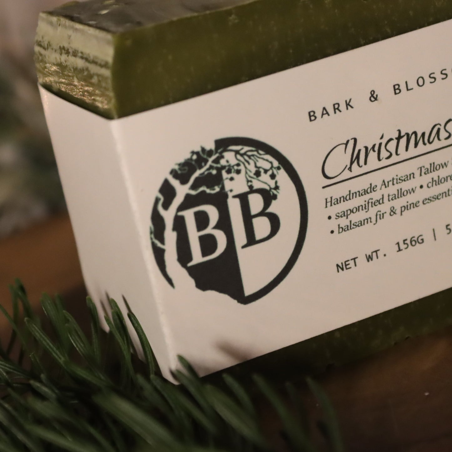 Bar of soap with 'Bark & Blossom' packaging on a wooden surface with greenery.